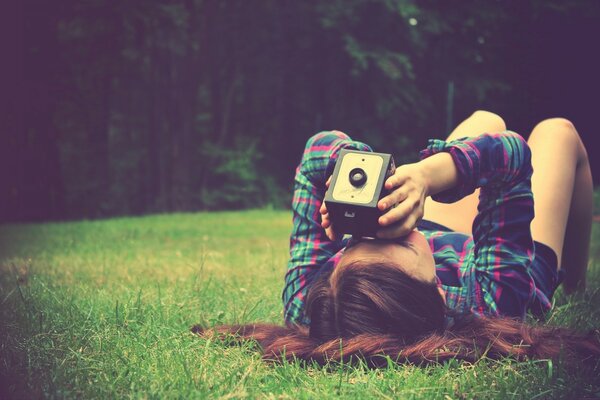 A girl is lying on the green grass and taking pictures