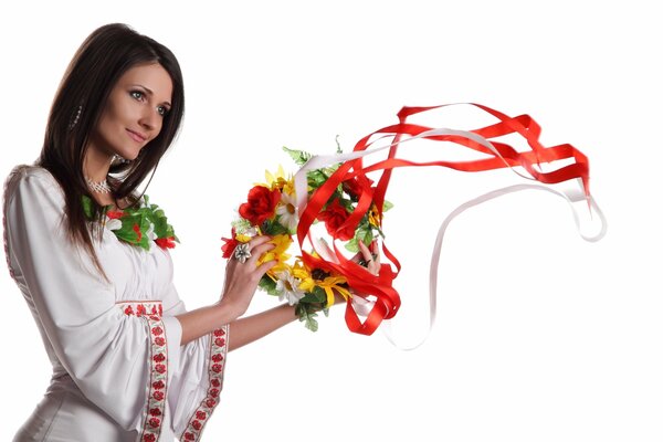 Una chica con una camisa blanca bordada sostiene una corona con cintas