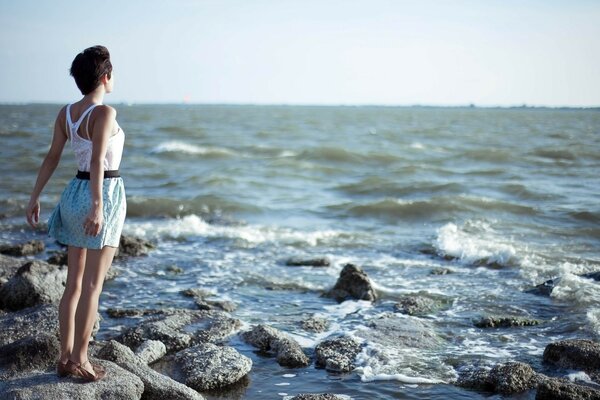 Chica de espaldas a las piedras de la orilla del mar