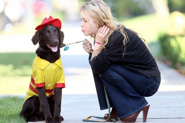 Perro en la ropa se sienta en la pista y a su lado la chica se inclinó