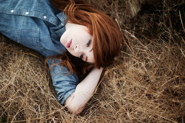 A red-haired girl is lying on the hay