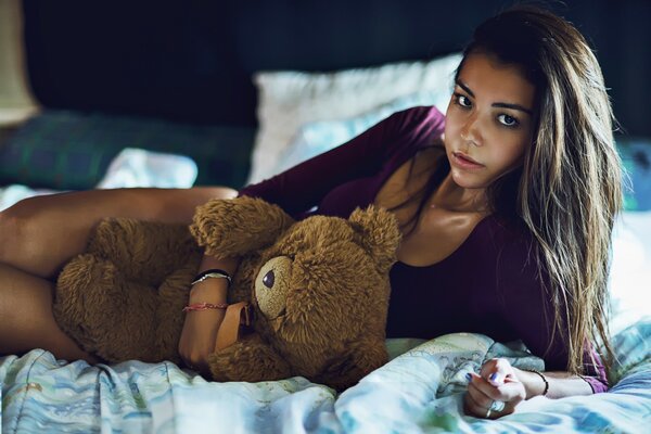 Fille se trouve sur le lit avec un ours jouet