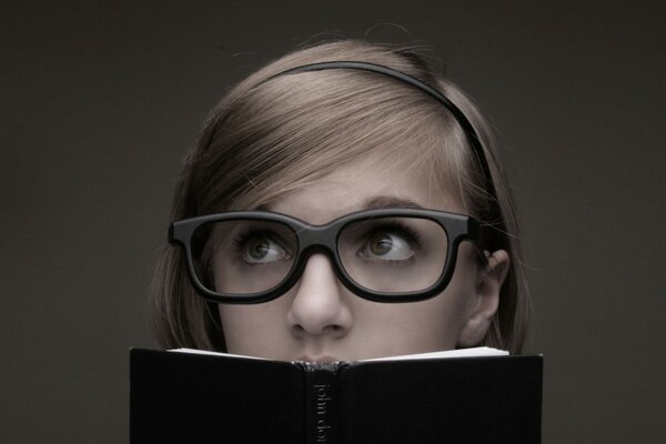 Chica con gafas enormes Mira encima de un libro