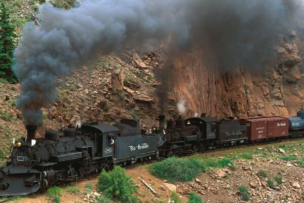 Black freight train rides on rails in the mountains