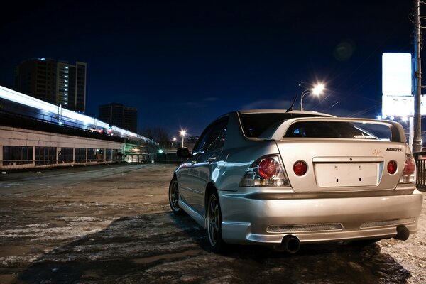 A new silver Toyota rides through the night city from behind