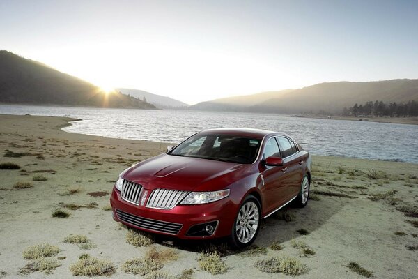 A red car is parked on a sandy beach