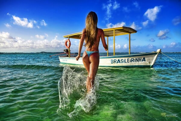 Chica va por el mar a un barco en bikini