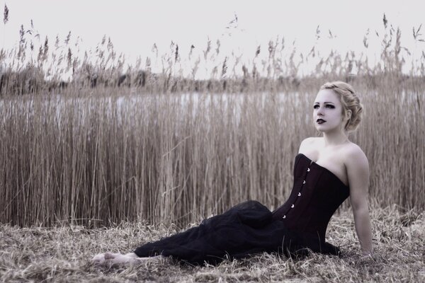 Pale blonde lying in a field in a black dress