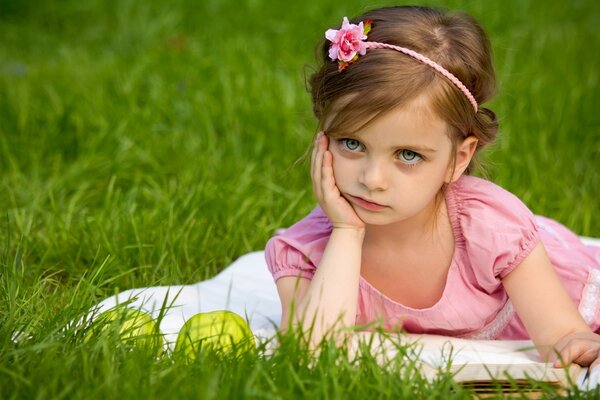 A child on the lawn with a book and apples in thought