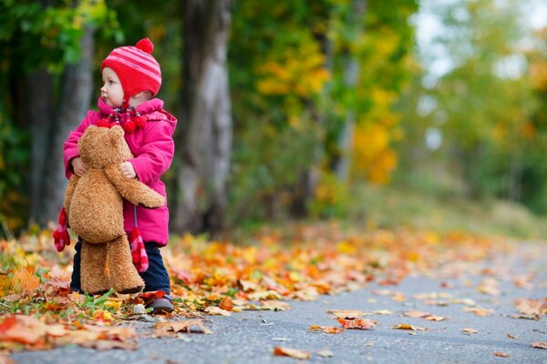 Un niño con un oso de peluche está de pie en el otoño