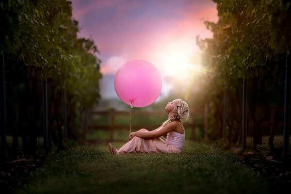 A girl with a pink ball sitting on the grass