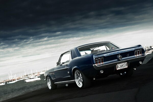 Ford Mustang standing on the embankment by the water with yachts against a cloudy gray sky