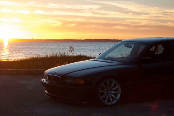 Bmw steht auf der Promenade am Wasser vor dem Hintergrund der untergehenden Sonne