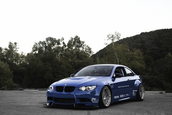 Vista frontal de un BMW azul contra un fondo de árboles