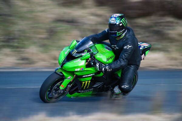 Un motociclista con casco en un Kawasaki verde entra en una curva