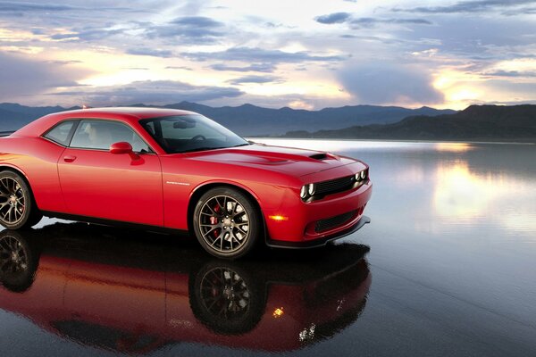 Red car in profile above the water