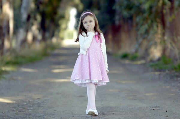 A girl with a headband in a pink dress on a forest path
