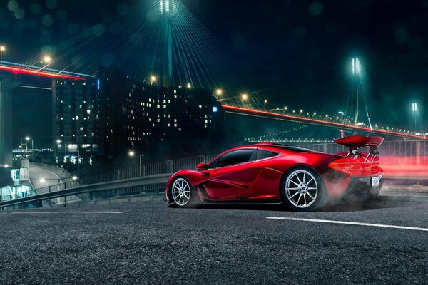 Red McLaren se précipite sur le pont à la lumière des lumières de la nuit. Une voiture de sport chère vole sur un pont de nuit