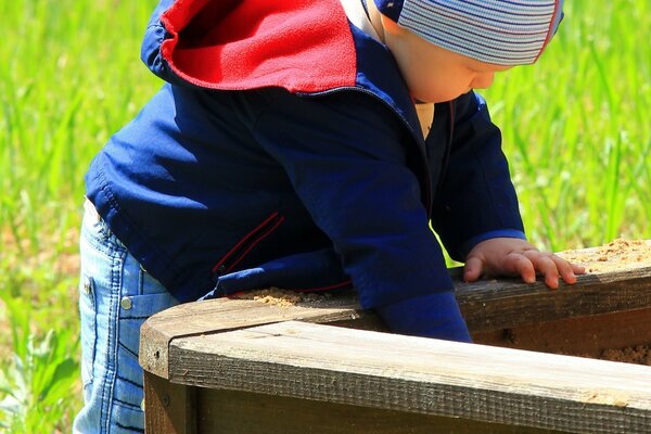 The boy climbs into the sandbox with his hands