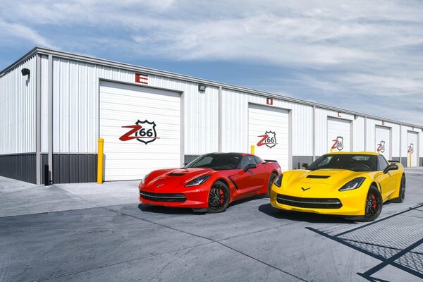 Coches deportivos brillantes en el fondo de los garajes bajo el cielo azul. Rojo y amarillo Chevrolet Corvette cerca de garajes