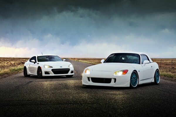 Two white cars with their headlights on on the highway