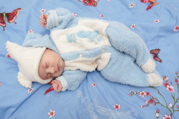 A baby boy on a blue bedspread with flowers