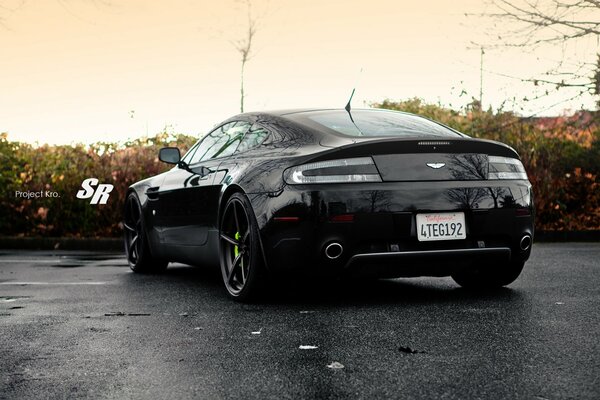 Voiture noire Aston Martin. Asphalte humide avec ciel coucher de soleil