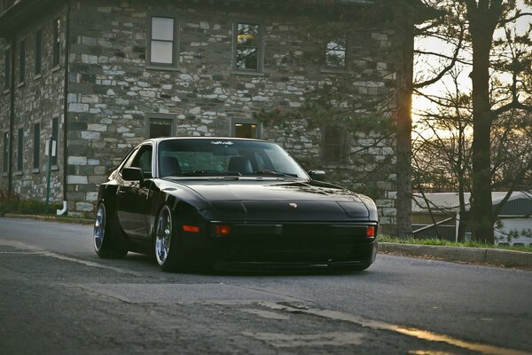 An old Black Porsche is driving down the road
