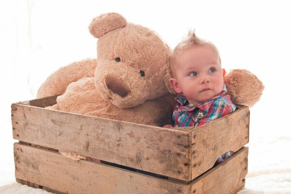 A boy with a teddy bear in a wooden box