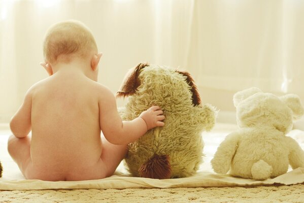 The baby is sitting in the same row with soft toys