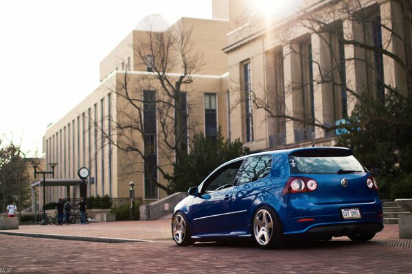 Blue Volkswagen golf rides in the city past the building