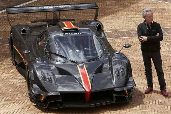 A man is standing next to a supercar. Pagani looks very impressive