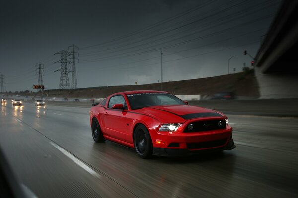 Coche Ford Mustang rojo en la carretera en medio de un cielo tormentoso