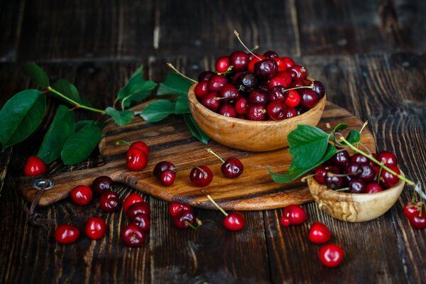 En una tabla de madera hay dos platos de madera con cerezas