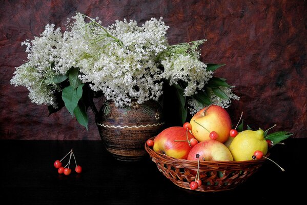 Sobre una mesa negra hay un jarrón con Lilas y una canasta con manzanas