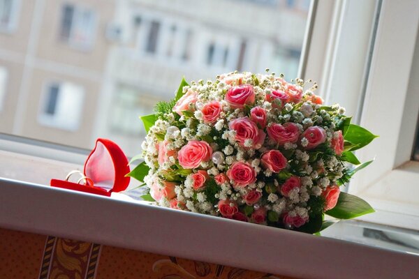 Brautstrauß aus Rosen und Trauringe in einer Schachtel auf der Fensterbank