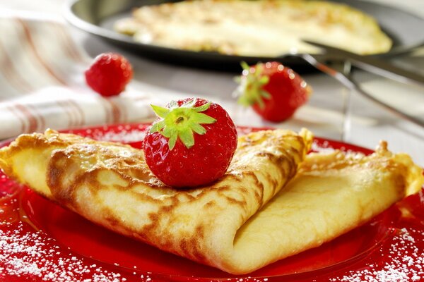 Pancake with strawberries on top on a red plate