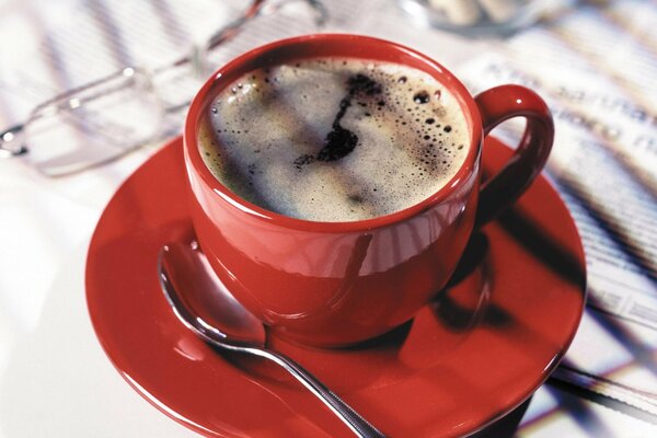 A cup of coffee in a red mug standing on the morning newspaper