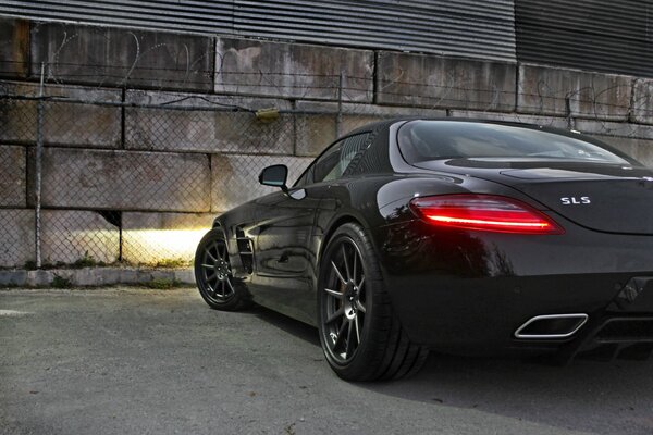 El Mercedes benz sls amg se encuentra contra una pared de bloques de concreto con los faros encendidos