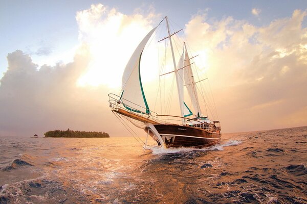 Navire avec des voiles blanches sur fond de coucher de soleil