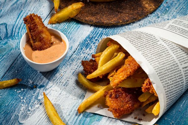 Les frites sont enveloppées dans un journal. Poisson trempé dans la sauce