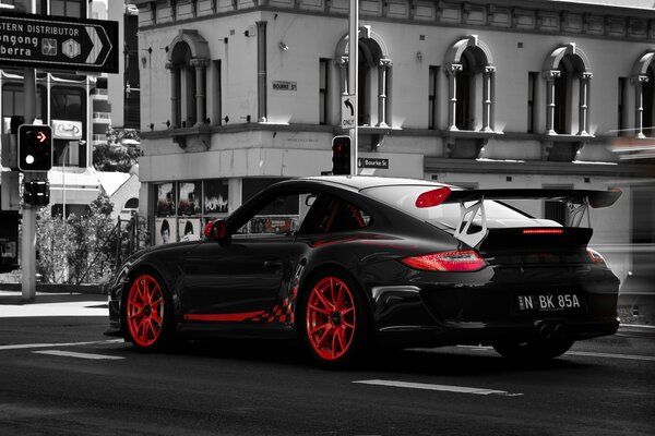 Porsche negro con Llantas rojas en una intersección de la ciudad