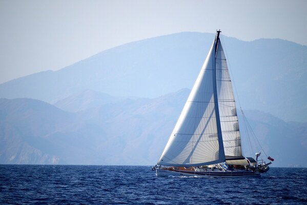 Against the background of the mountains - a yacht sailing on the sea