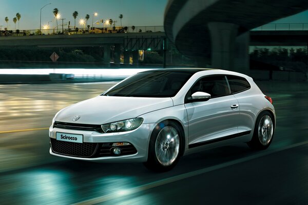 A white Volkswagen is driving along the highway at dusk