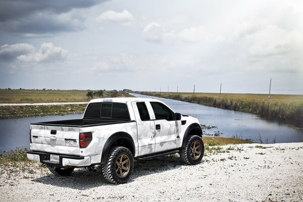 Pick-up blanc près de la rivière sous un ciel nuageux