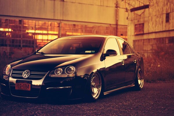 A tuned Volkswagen in black stands against the background of the factory