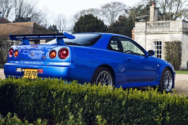 Nissan azul cerca de arbustos verdes en el fondo de una casa antigua