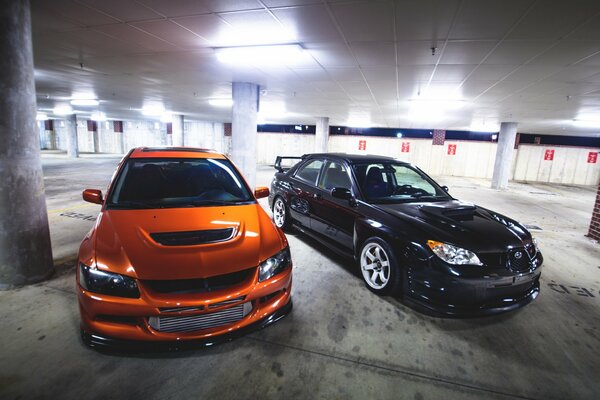 Mitshubishi naranja y subaru negro en el estacionamiento