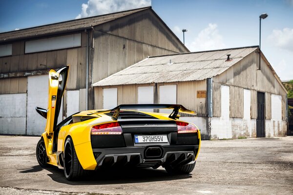 Yellow Lamborghini with an open door on the background of an old warehouse