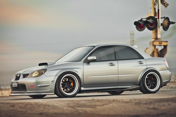 A silver subaru at a railway crossing